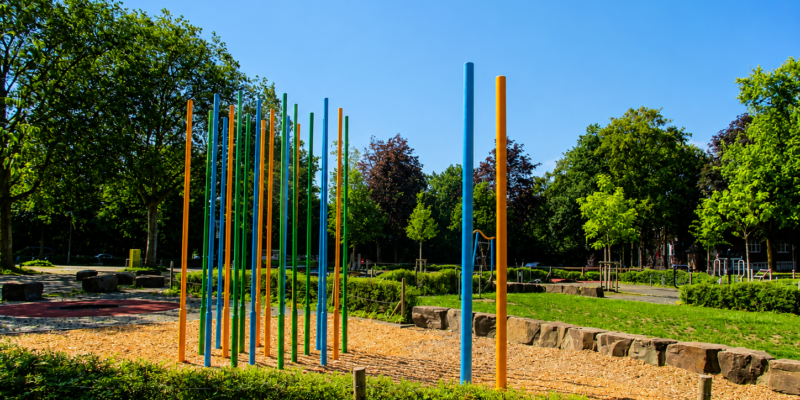 Ein Spielgerät auf einem Spielplatz, der von Hecken und Wiesen gesäumt ist.