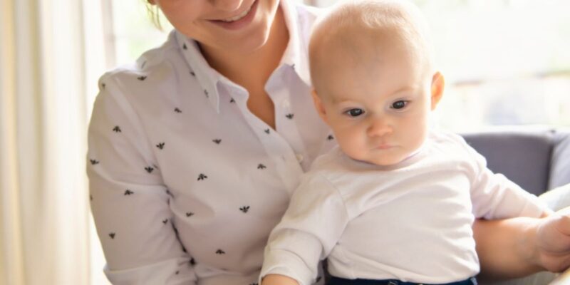 Eine Frau hat ein Baby auf dem Arm. Gemeinsam schauen sie in ein Buch.