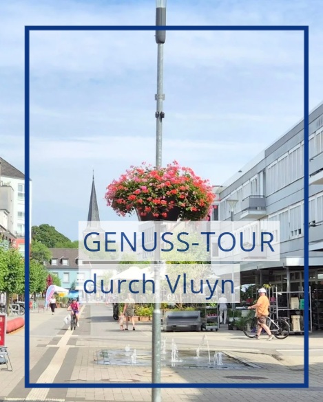 Eine Blumenampel ziert eine Straßenlaterne. Im Hintergrund erstreckt sich eine Fußgängerzone.
