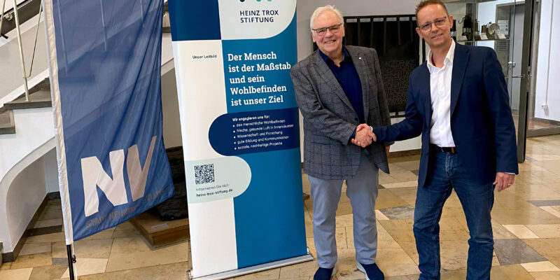 2 Männer stehen in einem Foyer und reichen sich die Hand.