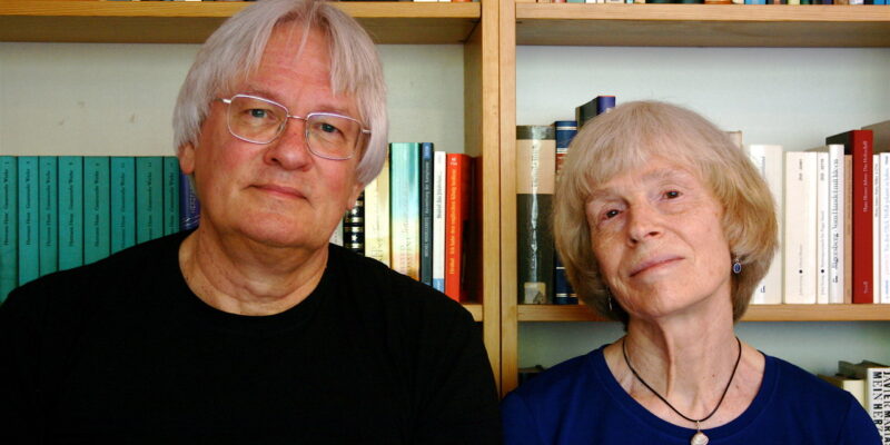 Ein Mann und eine Frau stehen vor einem Bücherregal und schauen in die Kamera.