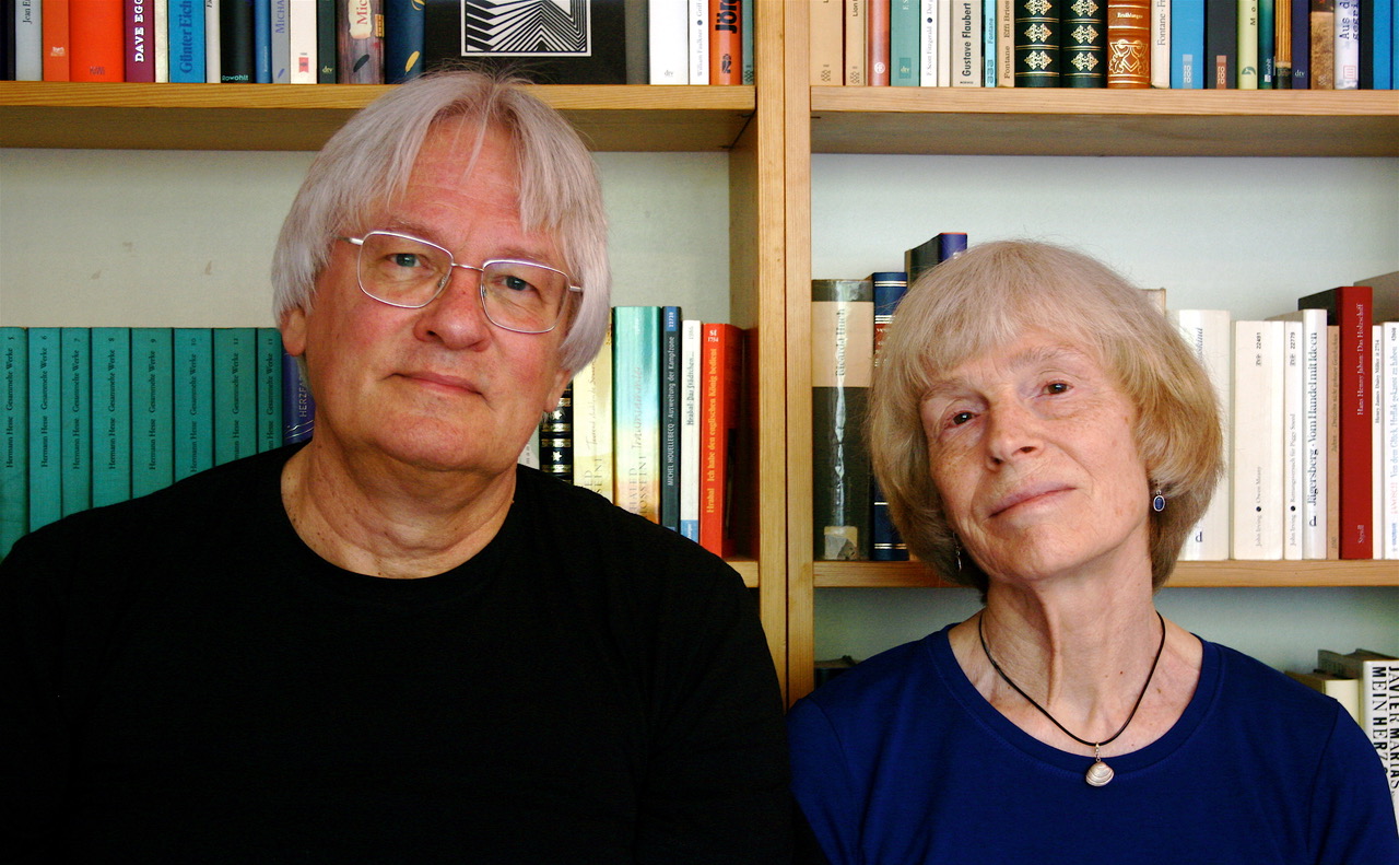 Ein Mann und eine Frau stehen vor einem Bücherregal und schauen in die Kamera.