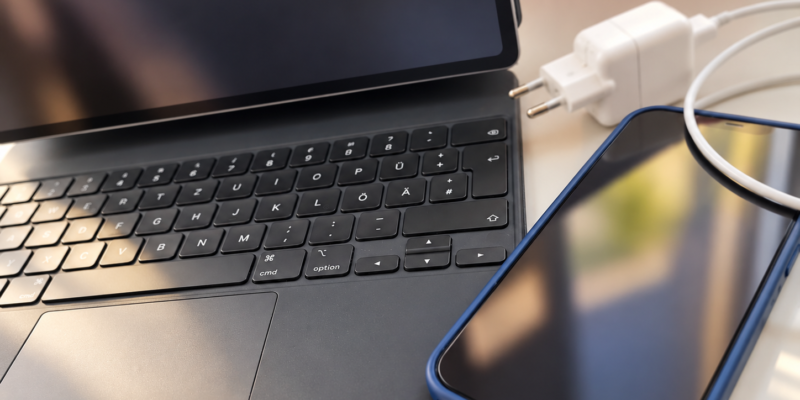 Ein Laptop, ein Smartphone und ein Ladekabel liegen auf einem Tisch.