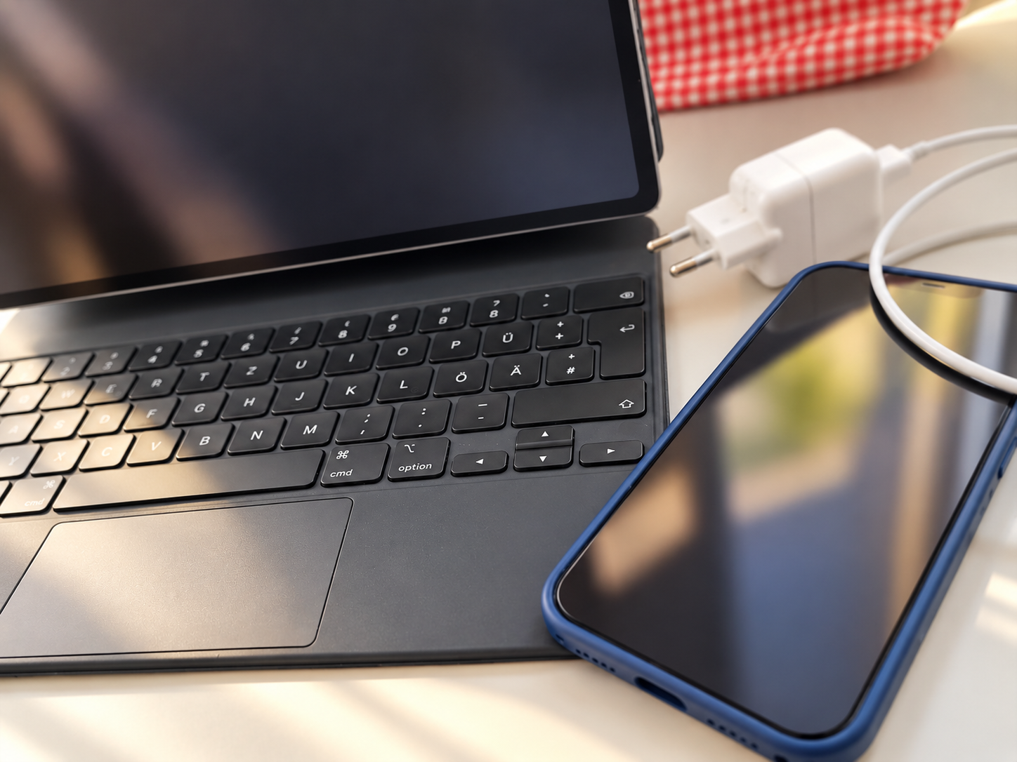 Ein Laptop, ein Smartphone und ein Ladekabel liegen auf einem Tisch.