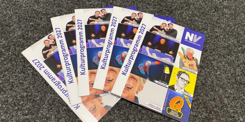 Fünf Programmhefte liegen aufgefächert auf dem Boden