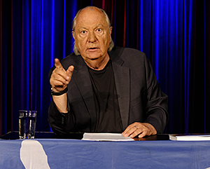 Ein Mann sitzt hinter einem Pult und zeigt mit dem Finger