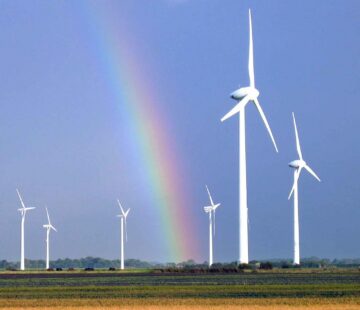 Mehrere Windenergieräder vor einem Regenbogen